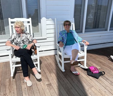 A picture of 2 women sitting in rocking chairs on the porch of the hotel.