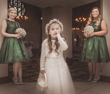 Young flower girl in white lace dress and flower crown standing with bridesmaids in green dresses.