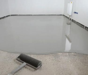 Freshly poured self-leveling floor compound with a spiked roller for smoothing gray epoxy.