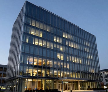 A wide-angle photograph of a prestigious international foundation headquarters with modern architecture and large glass windows, International / Global, dusk lighting with Silver and Dark Blue hues.