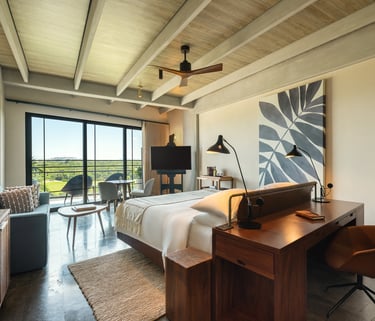 Modern luxury hotel suite with a wooden desk, king bed, and balcony overlooking a scenic landscape.