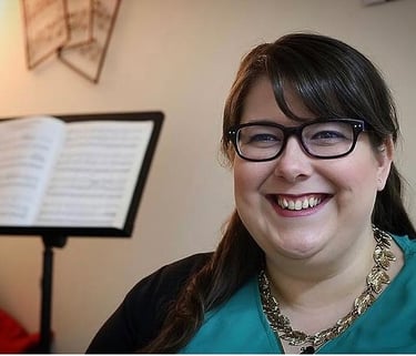 Laura is smiling just off camera and sitting in front of a music stand with music on it