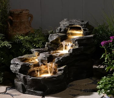 Illuminated rock waterfall fountain with cascading water and LED lights in a garden patio setting.