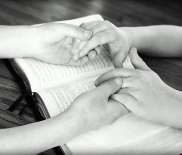 Hands held together over an open Bible in prayer.