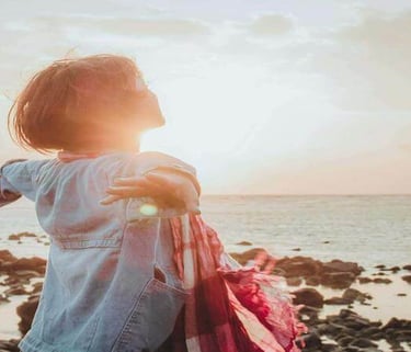 Person standing with arms open toward the sunrise, symbolizing freedom and new beginnings.