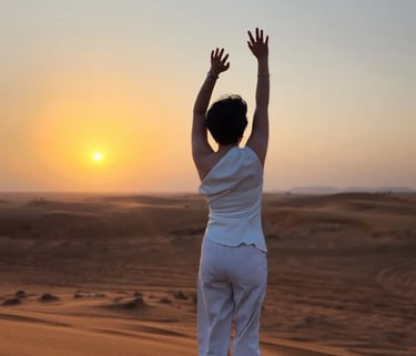A person seen from behind in the desert with arms in the air facing the sunset