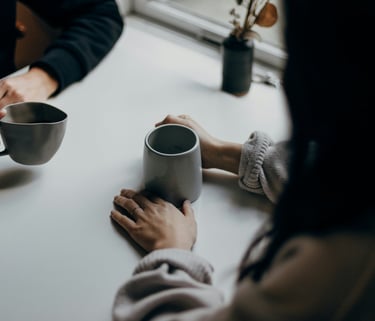 a therapist and client sit at a table, drinking coffee, having a private and empowering conversation