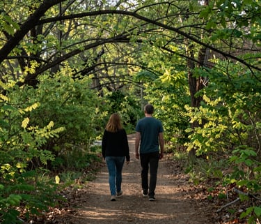 Two people walking along a nature trail in a North Houston park, surrounded by lush green spring foliage and soft morning light, photography.