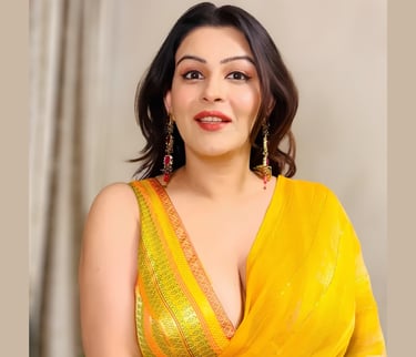 A woman in a vibrant yellow silk saree with gold borders and matching jewelry posing for a portrait.