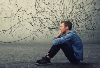 jeune  homme assis sur le bitume devant un mur envahie de graffiti et lignes noires
