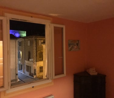 Chambre rustique à Quillan avec murs couleur terre cuite, lit double et fenêtre ouverte 