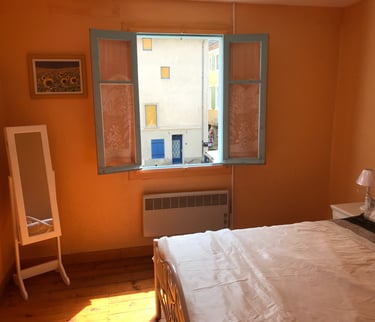 Chambre lumineuse à Quillan avec murs orange, miroir sur pied et grand lit près d’une fenêtre ensole