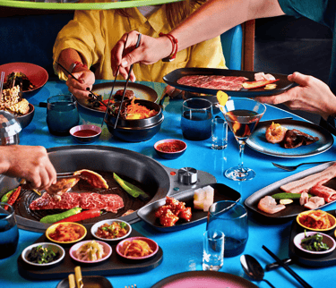 Friends dining at a Korean BBQ restaurant grilling Wagyu beef and enjoying traditional banchan side dishes.