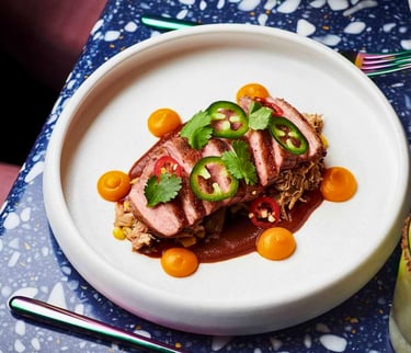 Seared duck breast sliced with mole sauce, jalapeños, and squash purée on a terrazzo table.