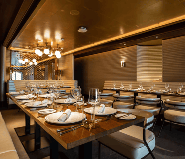 Elegant luxury cruise ship dining room with modern wooden tables and white leather chairs.