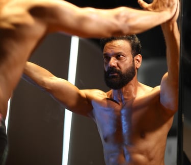 Shirtless man looking in mirror and evaluating himself and thinking about his fitness