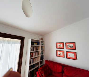 Living room with a red sofa, white bookshelf, and framed artwork on white walls.