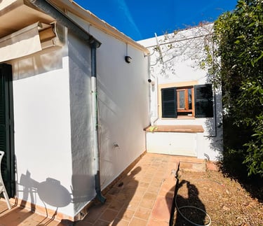 White stucco Mediterranean house patio with terracotta tile walkway and black window shutters.