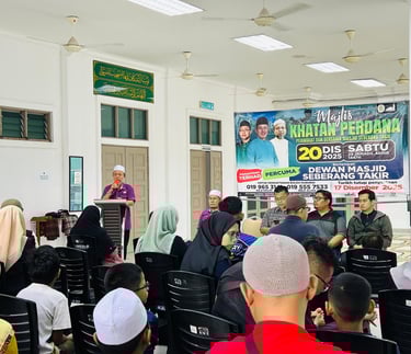 A community meeting at Dewan Masjid Seberang Takir with a speaker at a podium addressing an audience.