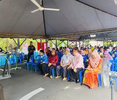 A community gathering under a large outdoor tent with speakers and seated audience members.