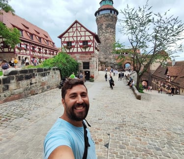 Smiling man taking a selfie at Nuremberg Castle with the Sinwell Tower and half-timbered houses.