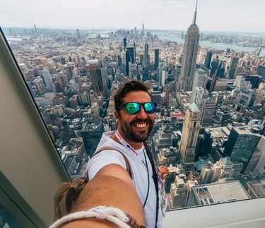 A smiling man takes a selfie with the Empire State Building and New York City skyline view.