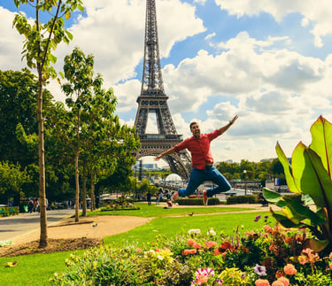 A happy man jumps in the air in front of the Eiffel Tower in Paris, France, on a sunny day.