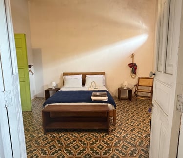 Rustic hotel room with vintage patterned tile flooring, a wooden bed with blue linens, and a bright lime green door.