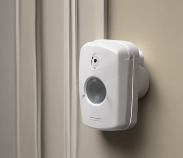 A scene of urban devastation featuring a severely damaged multi-story building with broken windows and a charred facade. The surrounding area is littered with debris and a wrecked car is parked among the rubble. A large tree stands near the building, and a few people are seen walking along the street.