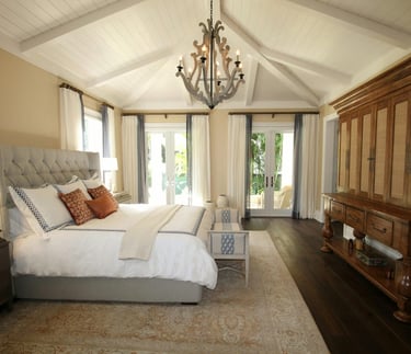 Elegant master bedroom with a vaulted ceiling, wood chandelier, and tufted headboard.