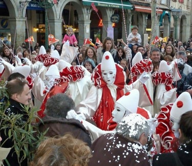 Crowd celebrates the Carnival of Limoux with performers in traditional red and white Pierrot costumes.