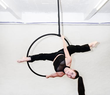 Vrouw in zwarte outfit voert een aerial hoop oefening uit bij De Polecats Fabriek in Gent