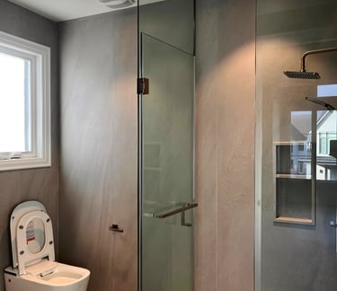 Modern bathroom with a glass walk-in shower, rain shower head, and sleek white toilet against gray tile walls.
