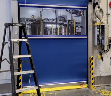 Blue industrial high-speed roll-up door with a clear vision panel installed in a warehouse facility.