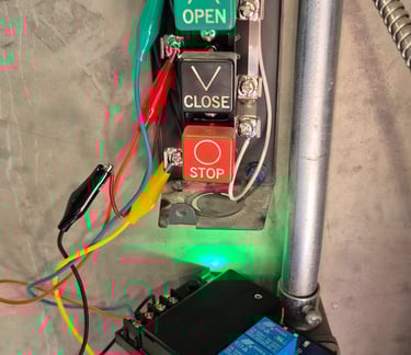 Industrial control station with open, close, and stop buttons wired to an electrical relay using alligator clips.