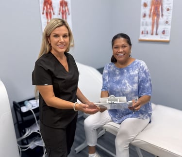 A smiling healthcare professional in black scrubs handing a medical clipboard to a patient in a clinic.
