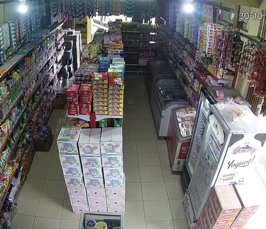 A fully stocked grocery store aisle with snack packets, beverage coolers, and boxes of food products.