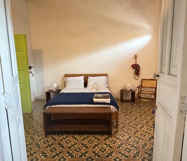 Rustic hotel room with vintage patterned tile flooring, a wooden bed with blue linens, and a bright lime green door.