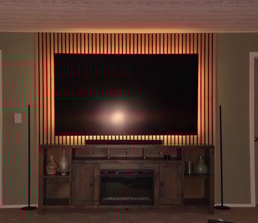 Modern wall-mounted TV with backlighting on a wood slat accent wall above a rustic fireplace console.