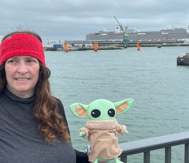 Woman holding little green companion standing at bridge with cruise ship in background