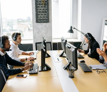 Smiling customer service representative wearing a headset, sitting at a desk with a computer