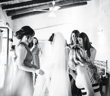 Fotografia in bianco e nero dei preparativi della sposa, mentre le amiche l'aiutano col velo dell'abito da sposa