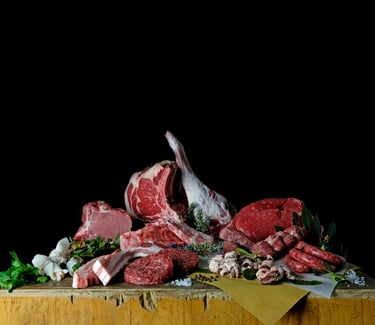 Variety of fresh raw meats including beef steaks, pork chops, and sausages on a rustic butcher block.