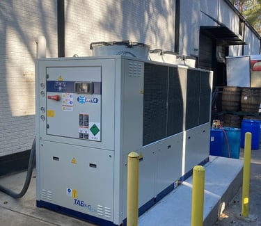 A large, industrial MTA TAEevo Tech chiller unit with multiple fans with wooden barrels behind