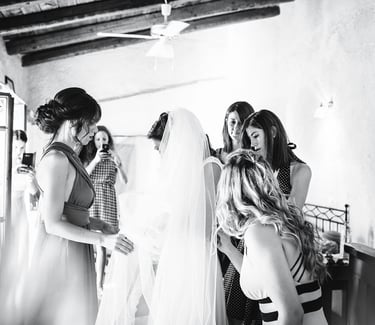 Fotografia in bianco e nero dei preparativi della sposa, mentre le amiche l'aiutano col velo dell'abito da sposa