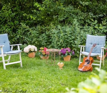 Zwei Stühle im Garten, eine Gitarre lehnt am Stuhl Blumen im Hintergrund