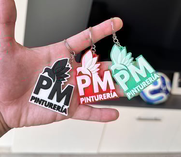 Custom 3D printed Pinturería PM logo  3d llaveros posadas in black, red, and green held in a hand.
