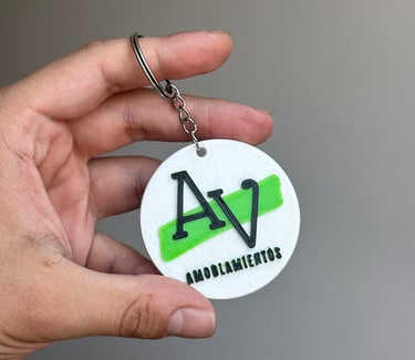 Custom 3D printed round keychain with black AV logo and green accent for Amoblamientos.