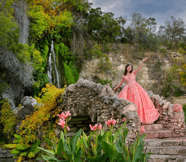 a woman in a pink quinceanera xv dress standing on a stone wall
