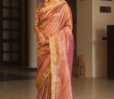 Elegant woman wearing a dusty pink organza silk saree with gold zari embroidery and statement earrings.